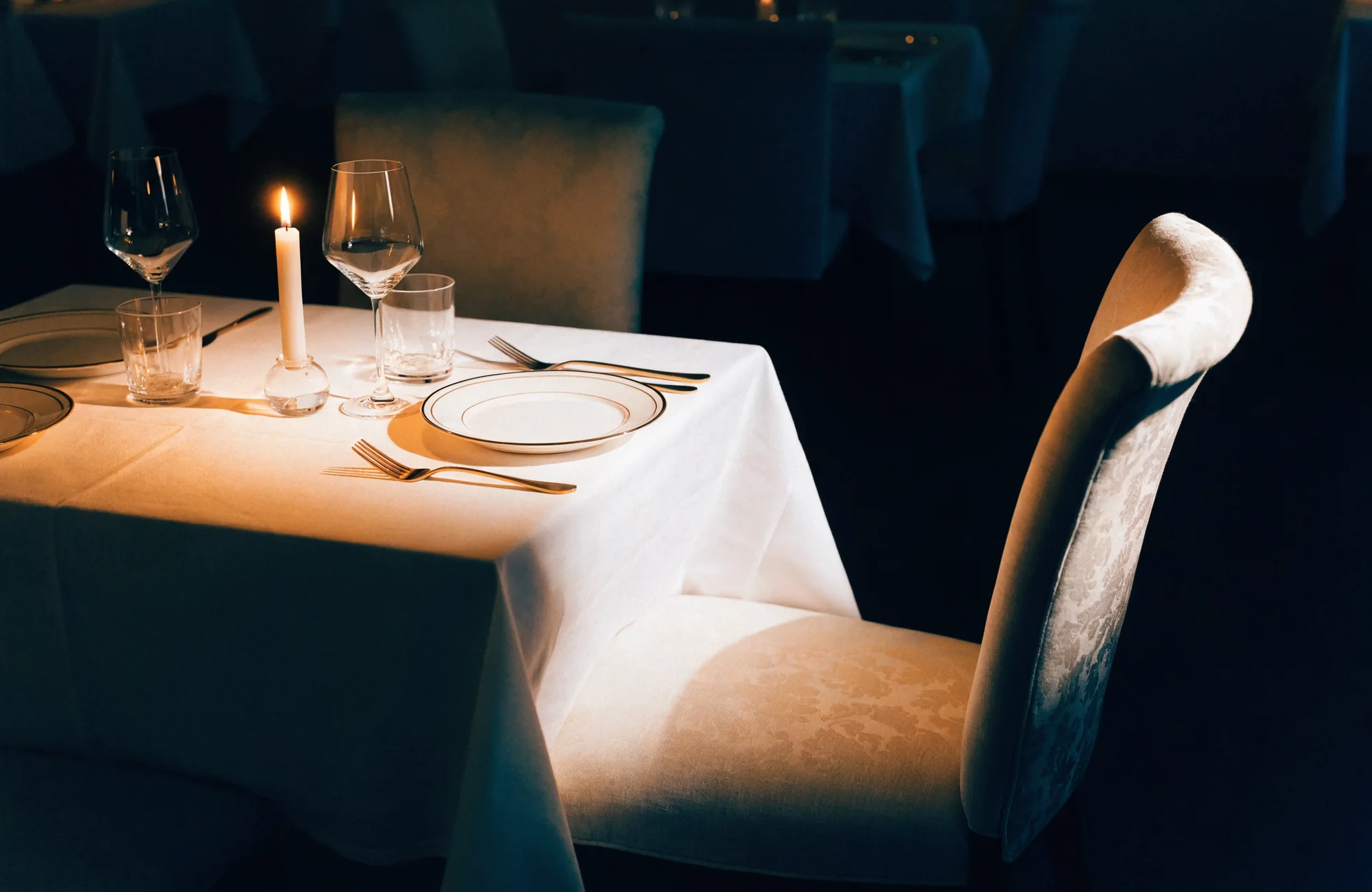 A candlelit table for two, one chair pulled out for the reader