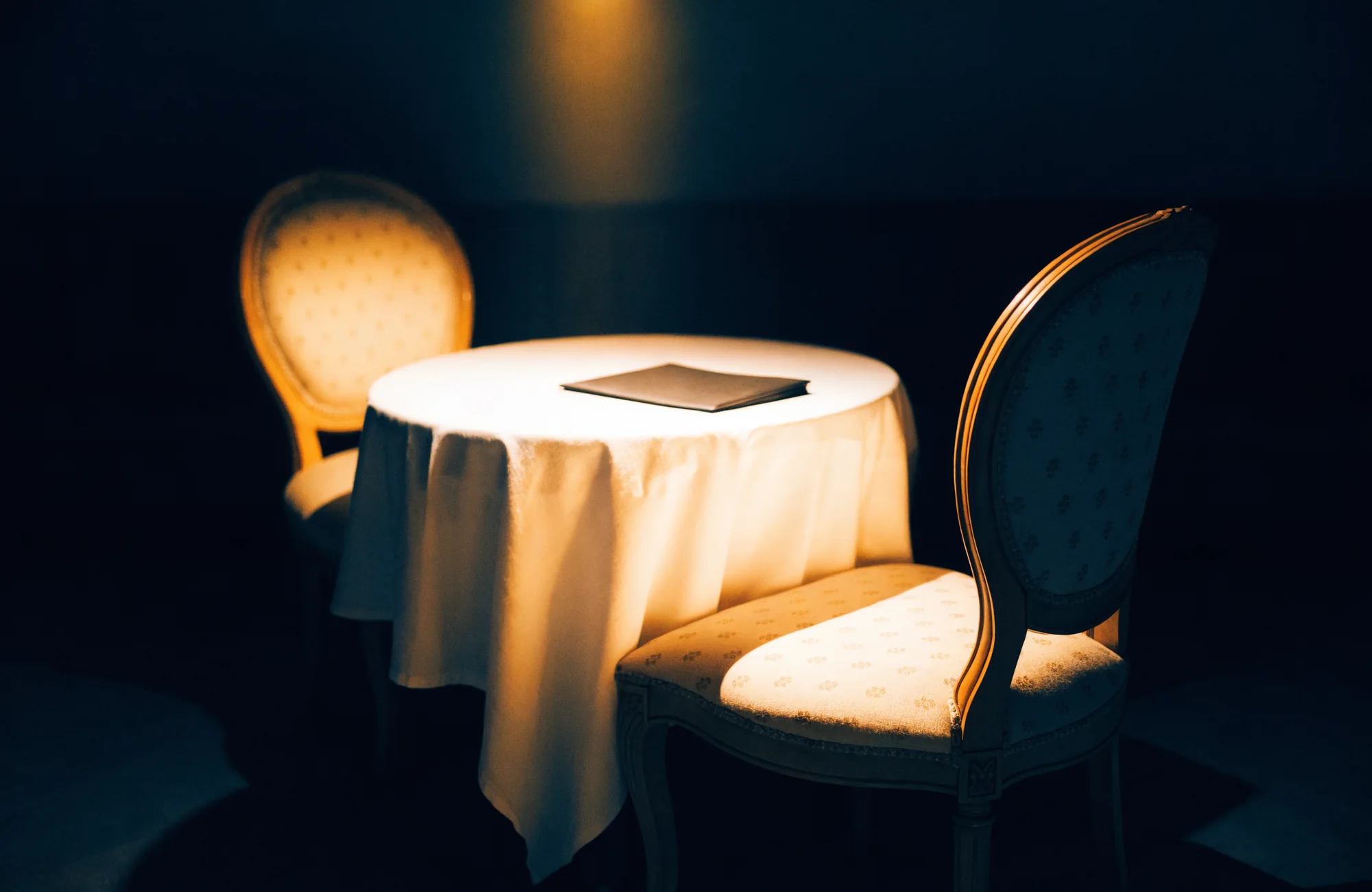 Two chairs at a table, one empty, an unopened folder